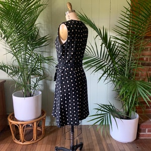 May include: A black and white patterned wrap dress with a sleeveless design. The dress has a square pattern and a tie at the waist.