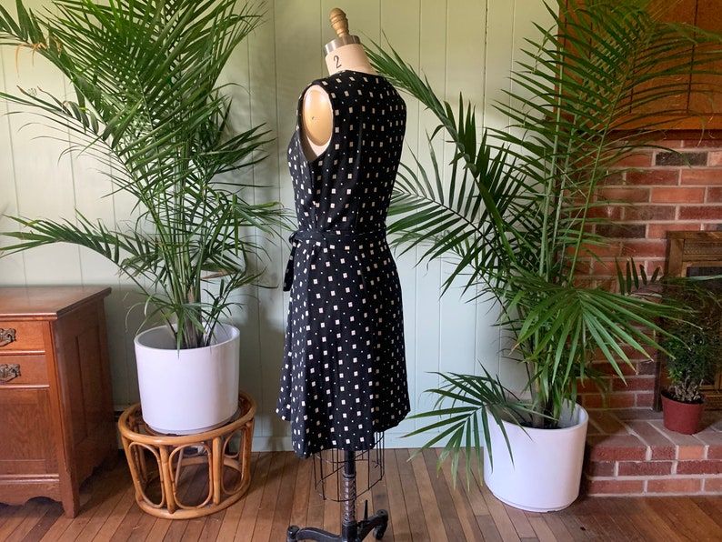 May include: A black and white patterned wrap dress with a sleeveless design. The dress has a square pattern and a tie at the waist.
