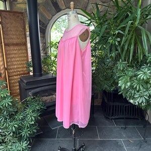 Puede incluir: Un camis&oacute;n rosa vintage en un maniqu&iacute;. El camis&oacute;n es de un rosa vibrante con un delicado ribete festoneado alrededor del escote y el dobladillo. La tela parece ligera y fluida, lo que sugiere un ajuste c&oacute;modo. El maniqu&iacute; se exhibe en una habitaci&oacute;n con plantas.
