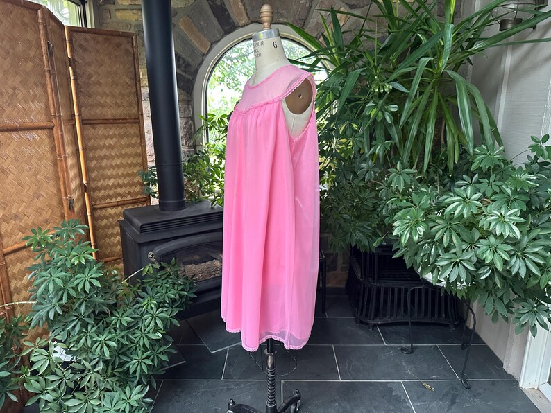 Puede incluir: Un camis&oacute;n rosa vintage en un maniqu&iacute;. El camis&oacute;n es de un rosa vibrante con un delicado ribete festoneado alrededor del escote y el dobladillo. La tela parece ligera y fluida, lo que sugiere un ajuste c&oacute;modo. El maniqu&iacute; se exhibe en una habitaci&oacute;n con plantas.