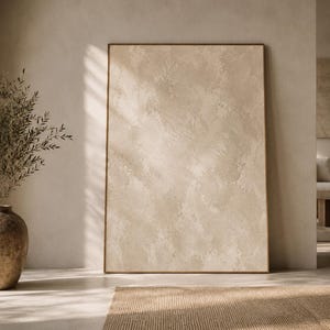 Pode incluir: Uma grande obra de arte abstrata emoldurada com uma paleta de cores neutras. A obra de arte é exibida em uma sala bem iluminada com um vaso de plantas secas e um tapete tecido. A moldura é de cor marrom quente.