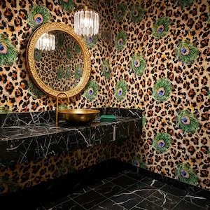 May include: A luxurious bathroom with a black marble countertop and floor. A gold-colored sink and faucet are set against a wall with a leopard print and peacock feather design. A round gold mirror and a crystal chandelier complete the look.