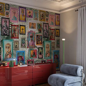 以下が含まれることがあります： 鮮やかな色の額入り動物の肖像画が飾られたギャラリーウォールのある部屋。赤いドレッサーと青いアームチェアが前景にあります。壁紙は熱帯の葉の模様です。