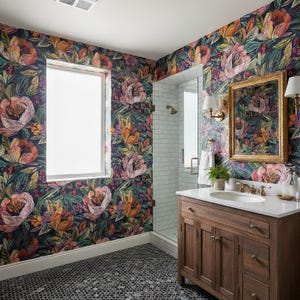 May include: A bathroom with floral wallpaper in shades of pink, orange, and green. The room features a wooden vanity with a white countertop, a framed mirror, and a shower with white tiles.