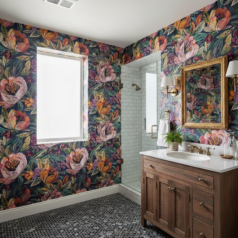 May include: A bathroom with floral wallpaper in shades of pink, orange, and green. The room features a wooden vanity with a white countertop, a framed mirror, and a shower with white tiles.
