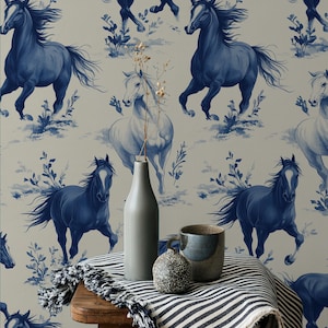Peut inclure: Un motif de papier peint avec un motif répété de chevaux bleus courant sur un fond neutre. La scène comprend un tabouret en bois, une couverture à rayures, un vase, une tasse et une pierre décorative.