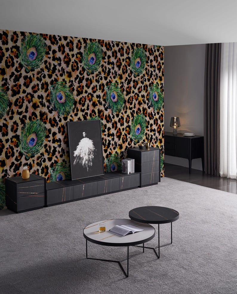 May include: A modern living room featuring a black entertainment center with a marble-like top, two round coffee tables, and a wall with a leopard print and peacock feather design. A framed artwork is displayed on the entertainment center.
