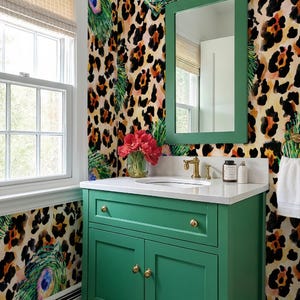 May include: A green bathroom vanity with gold hardware and a white countertop. The vanity is set against a wall with a leopard print and peacock feather design. A mirror with a green frame hangs above the vanity.