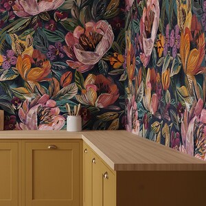 May include: A kitchen corner with mustard-yellow cabinets and gold handles, topped with a light wood work surface. The walls are decorated with dark floral wallpaper in pink, orange, and green, creating a colourful and stylish space.