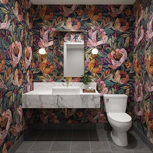 May include: A bathroom with floral wallpaper in shades of pink, orange, and green. The room features a white marble vanity with a rectangular sink, a gold-framed mirror, and a white toilet. Two wall lights flank the mirror.
