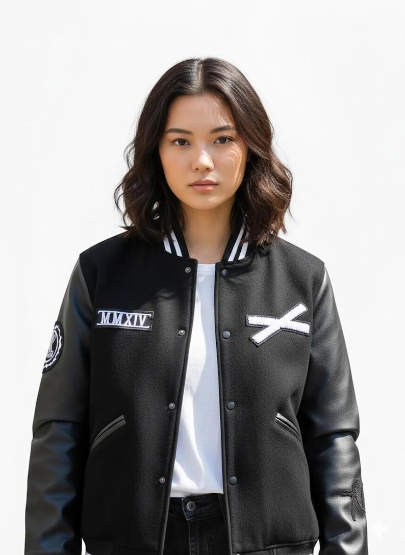 K&ouml;nnte beinhalten: Schwarze Collegejacke mit wei&szlig;en Akzenten, Leder&auml;rmeln und einem wei&szlig;en "X" Aufn&auml;her. Die Jacke hat einen wei&szlig;en Kragen mit schwarzen Streifen und einen Aufn&auml;her mit der Aufschrift "MMXIV".