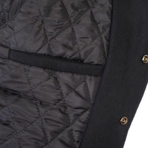 K&ouml;nnte beinhalten: Nahaufnahme des Innenraums einer schwarzen Jacke. Das Futter ist rautenf&ouml;rmig gesteppt. Eine schwarze Tasche ist sichtbar. Der &auml;u&szlig;ere Rand der Jacke ist schwarz mit goldfarbenen Druckkn&ouml;pfen.