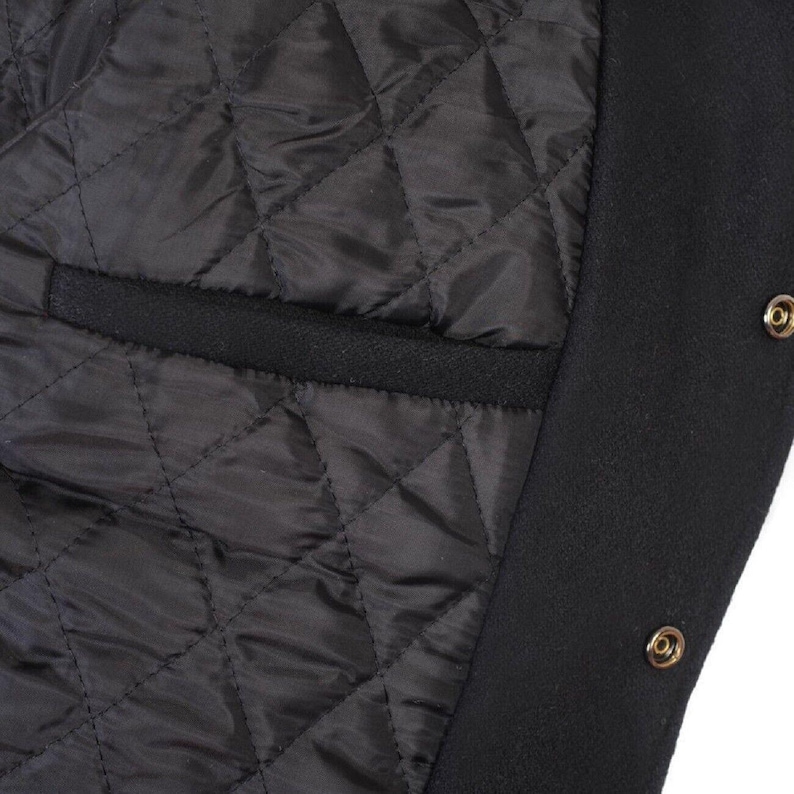 K&ouml;nnte beinhalten: Nahaufnahme des Innenraums einer schwarzen Jacke. Das Futter ist rautenf&ouml;rmig gesteppt. Eine schwarze Tasche ist sichtbar. Der &auml;u&szlig;ere Rand der Jacke ist schwarz mit goldfarbenen Druckkn&ouml;pfen.