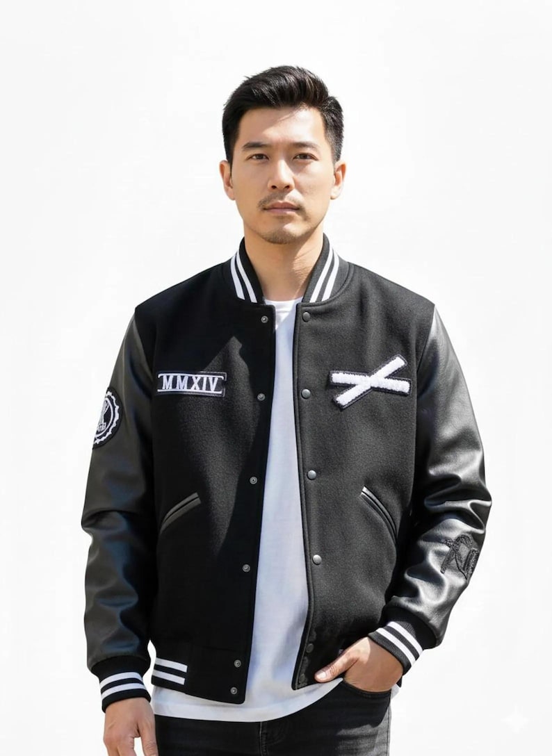 K&ouml;nnte beinhalten: Schwarze Collegejacke mit wei&szlig;en Akzenten, Leder&auml;rmeln und Knopfleiste. Die Jacke hat wei&szlig;e Aufn&auml;her mit der r&ouml;mischen Zahl MMXIV und einem wei&szlig;en X. Die Manschetten und der Kragen haben wei&szlig;e Streifen.