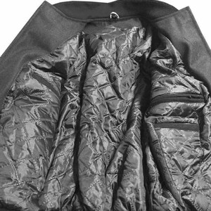K&ouml;nnte beinhalten: Nahaufnahme des Inneren eines dunkelgrauen Mantels. Das Innere des Mantels hat ein gestepptes, schwarzes Futter mit einem Rautenmuster. Der Mantel hat zwei Taschen und einen Kragen mit einer Metallschlaufe.