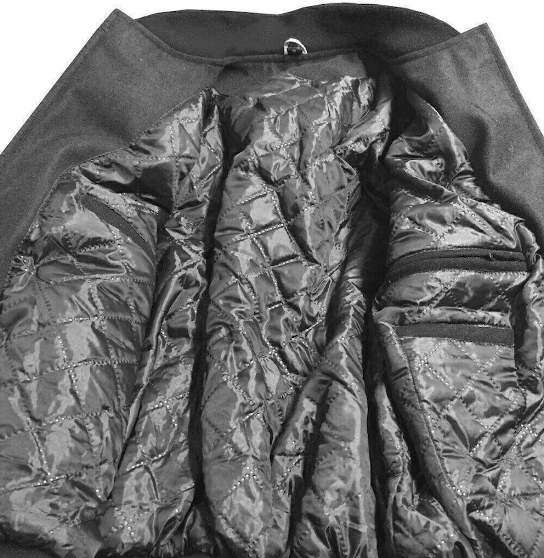 K&ouml;nnte beinhalten: Nahaufnahme des Inneren eines dunkelgrauen Mantels. Das Innere des Mantels hat ein gestepptes, schwarzes Futter mit einem Rautenmuster. Der Mantel hat zwei Taschen und einen Kragen mit einer Metallschlaufe.