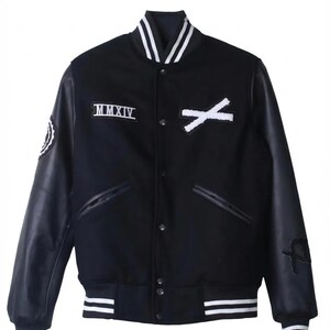 K&ouml;nnte beinhalten: Schwarze Collegejacke mit wei&szlig;en Akzenten. Sie hat schwarze Leder&auml;rmel, einen wei&szlig;en Kragen und wei&szlig; gestreifte S&auml;ume und B&uuml;ndchen. Enth&auml;lt die r&ouml;mische Zahl "MMXIV" und ein wei&szlig;es "X"-Design auf der Brust.