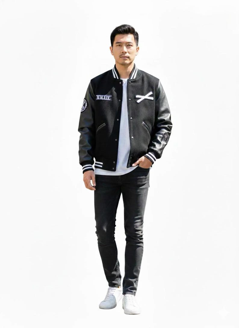 K&ouml;nnte beinhalten: Eine schwarze Collegejacke mit Leder&auml;rmeln, wei&szlig;en Streifen und Aufn&auml;hern. Die Jacke wird &uuml;ber einem wei&szlig;en T-Shirt getragen und mit schwarzen Jeans und wei&szlig;en Turnschuhen kombiniert. Die Jacke hat den Text "MMXIV" auf der Brust.