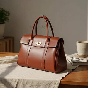 May include: A tan leather handbag with a structured design. The bag features a top handle, a flap closure with a gold-coloured clasp, and vertical stitching details. The bag is sitting on a wooden table.