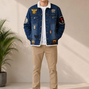 Peut inclure: Une veste en jean bleu avec un col et une doublure en sherpa blanc, ornée de divers écussons brodés, portée sur un t-shirt blanc uni et un pantalon beige. La veste présente un écusson aigle doré, une lettre T rouge et d'autres motifs.