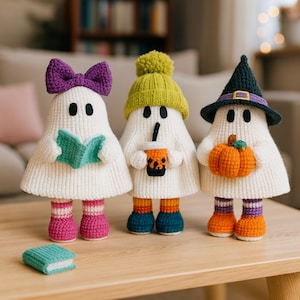 May include: Three handmade crochet ghost figures with unique accessories. One ghost wears a purple bow and holds a book, another has a green hat and a drink, and the last wears a witch hat and holds a pumpkin. They are on a wooden table.