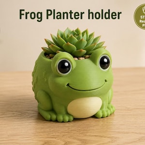 May include: A green frog-shaped planter holder with large black eyes and a cream-colored belly, containing a green succulent plant. The text "Frog Planter holder" and a circular badge stating "STL File Ready to PRint" are visible.
