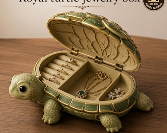 May include: A green and gold turtle-shaped jewelry box with an open hinged lid. The interior features a ring holder section with four rings and a compartment containing a gold chain necklace with a green pendant and small flower-shaped earrings.