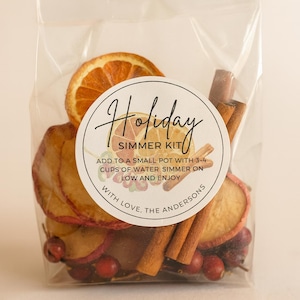 May include: A clear cellophane bag filled with dried orange slices, apple slices, cinnamon sticks, and cranberries. A round label reads "Holiday Simmer Kit" with instructions. The kit is designed to be simmered in water.