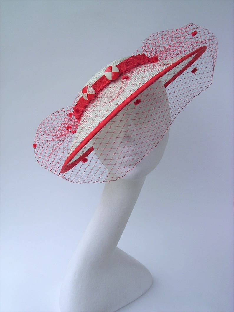 May include: A white straw hat with a red ribbon and red netting. The hat has a red and white polka dot trim.