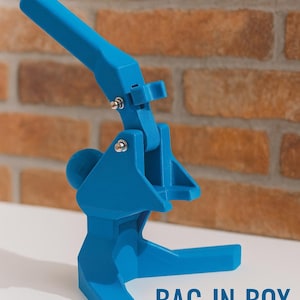 Puede incluir: Un soporte azul brillante para bag-in-box con un diseño articulado. El soporte es de plástico y tiene una base, un brazo de soporte y un mecanismo de inclinación. El texto "BAG-IN-BOX STAND" está impreso en blanco.