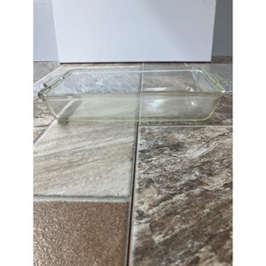 Puede incluir: Una fuente de horno rectangular de vidrio transparente con un interior dividido. La fuente tiene asas pequeñas en cada extremo. La fuente está sobre una superficie embaldosada.