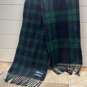 May include: A long rectangular scarf featuring a dark navy blue and forest green plaid tartan pattern. The scarf has fringed ends and a rectangular fabric label near one edge that reads Polo Ralph Lauren in white text on a dark blue background.