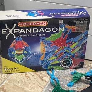 May include: A Hoberman Expandagon construction system basic kit box featuring colourful plastic building parts in red, blue, green, and yellow. The packaging displays the product name, age recommendation of 8 and up, and includes over 35 parts.