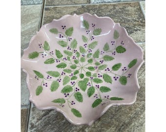Bol de cerámica rosa con borde festoneado, pintado a mano con hojas verdes y bayas moradas.