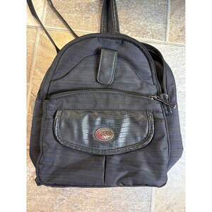 May include: Black backpack with a textured, striped design. Features a front pocket with a faux-leather, reptile-like texture and a silver emblem. Includes a top handle and adjustable straps.