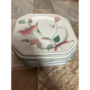 Puede incluir: Una pila de platos octogonales de color blanco roto con un acabado moteado y un diseño floral pintado con flores rosas y hojas verdes. Cada plato tiene un borde fino de color verde oscuro, creando un conjunto de vajilla uniforme.