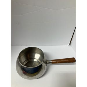 May include: A stainless steel saucepan with a wooden handle. The pan has a rounded body and a spout for easy pouring. The handle is made of dark brown wood and is attached to the pan with a metal bracket.