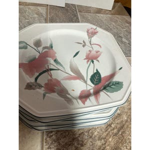 Puede incluir: Una pila de platos octogonales de cerámica blanca con un patrón floral de flores rosas, hojas verdes y finos bordes de color verde oscuro. El diseño incluye varias flores similares a rosas y follaje sobre la superficie de cada plato.