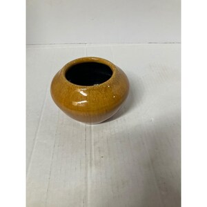 Op de afbeelding: Een kleine, ronde keramische vaas met een glanzende, gespikkelde, bruinachtige buitenkant en een zwarte binnenkant. De vaas heeft een brede opening en een afgeronde body. Het is een decoratief item.