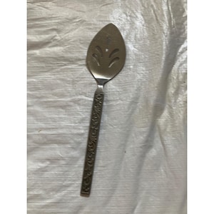 May include: A silver-colored pie server with a decorative handle. The server has a slotted, leaf-shaped blade with three decorative cutouts. The handle features an embossed floral design.