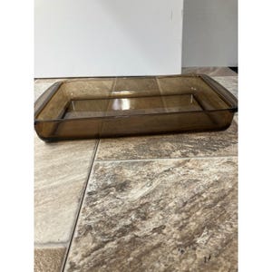 Könnte beinhalten: Eine rechteckige, bernsteinfarbene Glasbackform. Die Form hat eine leicht abgerundete rechteckige Form mit flachem Boden und geraden Seiten. Das Glas ist transparent und ermöglicht die Sichtbarkeit des Inhalts. Für den Ofen geeignet.