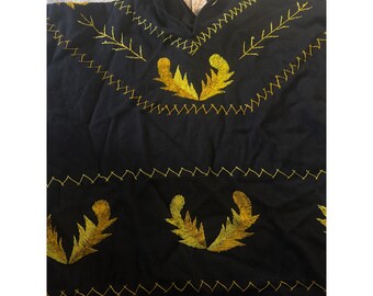 Poncho de lana bordado a mano con flecos y motivos de plumas negras y doradas.