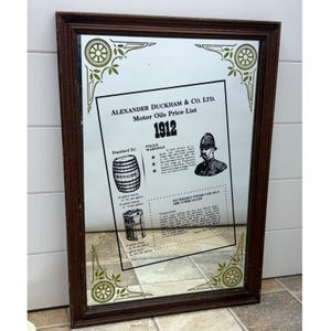 Peut inclure: Miroir rectangulaire avec un cadre en bois brun foncé. La surface du miroir reflète une publicité vintage pour les huiles moteur Alexander Duckham & Co. Ltd. de 1912, avec texte et illustrations. Des accents décoratifs verts et dorés ornent les coins.