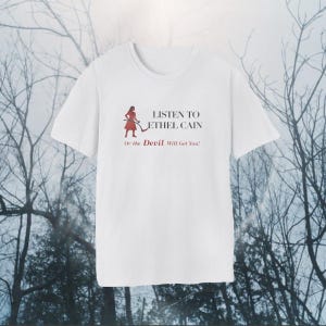 Peut inclure: Un t-shirt blanc à manches courtes avec un motif représentant une personne en robe rouge tenant une faux. Le texte indique : LISTEN TO ETHEL CAIN Or the Devil Will Get You ! Le t-shirt possède un col rond et une coupe standard unie au dos.