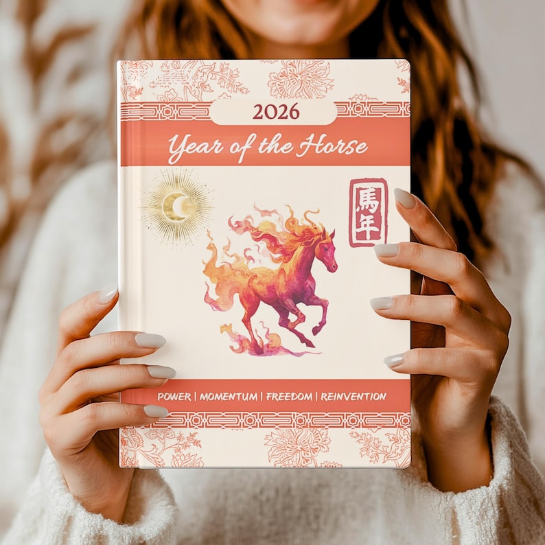 A cream-colored 2026 Year of the Horse journal. The cover features a watercolor illustration of a fiery horse, a crescent moon, and the text "Year of the Horse". The journal also includes the words "Power | Momentum | Freedom | Reinvention".