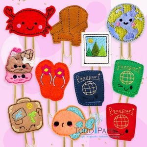 May include: Set of ten colorful felt clip-on bookmarks with various travel themes, including a crab, a beach chair, a passport, a suitcase, flip-flops, a fish, a globe, and a camera. Each bookmark has a cute cartoon face.
