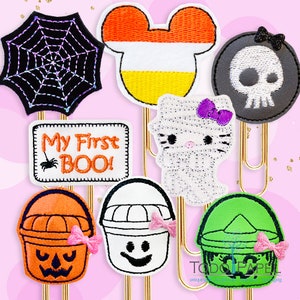 Może przedstawiać: Zestaw dziesięciu spinaczy do papieru w stylu Halloween z różnymi wzorami, w tym pajęczyna, głowa Myszki Miki z kukurydzy cukrowej, czaszka, duch, wiaderko z twarzą dyni, wiaderko z twarzą ducha, wiaderko z twarzą potwora i tabliczka z napisem "My First Boo!"