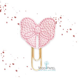 May include: A pink leather bow paper clip with a gold metal clip. The bow is stitched with a white thread.  "TODO PAPEL" is printed in black text on a white background below the clip.  "unique gifts, scrapbooks, stationery, packaging" is printed in black text below the logo.