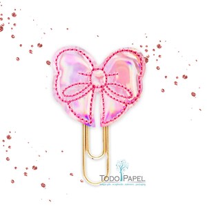 May include: A gold paper clip with a pink iridescent bow attached to the top. The bow has a pink stitched outline.