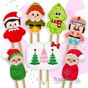 Puede incluir: Conjunto de seis clips de papel con temática navideña que presentan una variedad de personajes, incluidos elfos, un árbol de Navidad y un cascanueces. Los clips de papel son de color dorado y tienen un diseño festivo.